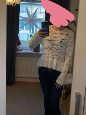 Vit stickad tröja med volangkant - Säljer en söt vit stickad tröja med hålmönster och volangkant nedtill. Tröjan har lång ärm och rund halsringning, perfekt för dig som gillar en feminin och trendig stil. Passar lika bra till jeans som till kjol.