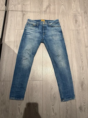 Blå tapered jeans från Jack & Jones - Snygga blå jeans från Jack & Jones med tapered passform, modellen Mike. Klassisk femficksdesign, ljus tvätt och kontrastsömmar. Jeansen har en normal midja och är gjorda i slitstarkt bomullsmaterial. Perfekt för dig som gillar en modern och avslappnad stil.