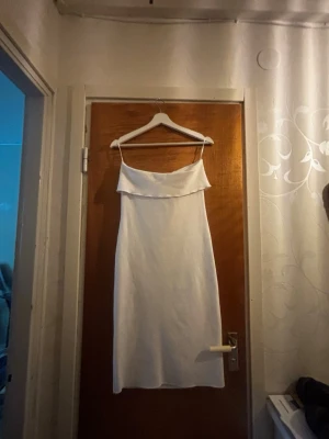 Vit långklänning med smala axelband - Säljer en stilren vit långklänning med smala axelband och en snygg draperad överdel. Klänningen har en rak siluett och är ärmlös, vilket ger en elegant och modern look. Perfekt för dig som gillar minimalistisk stil och ljusa färger.