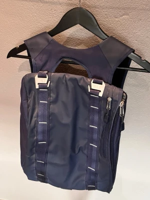 Db blå ryggsäck - Säljer en stilren marinblå ryggsäck från Db med smarta fack och robusta axelremmar. Väskan har två dragkedjor på sidan, metallspännen och ett stort innerfack med mesh.  