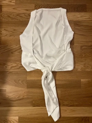 öppenrygg Vit omlott topp  - Säljer en vit omlott topp från Zara i storlek M. Toppen är ärmlös och har en snygg knytning framtill som ger en cool och modern look. oanvänd 