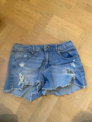 Blå jeansshorts från Denim Collection - Säljer ett par blå jeansshorts från Denim Collection med slitna detaljer och fransiga kanter. Pris kan diskuteras. Säljer då dom inte passar mig längre.