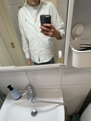 Vit skjorta från Ralph Lauren - Klassisk vit skjorta från Ralph Lauren med broderad logga på bröstet. Skjortan har knappar hela vägen, button down-krage och långa ärmar. Tillverkad i mjuk bomull och har en clean, tidlös look som funkar till allt.