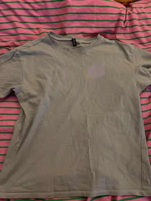  Grå t-shirt  - Säljer en Grå t-shirt från Cropp med stort retroinspirerat tryck på ryggen.  Klassisk passform och rund halsringning. Perfekt för att ta på sig när man ska till stranden över badkläderna Elelr som en najs snygg everyday tröja😜