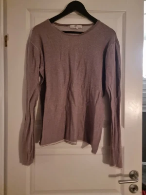 Ljusbrun stickad tröja från HOPE - Säljer en ljusbrun stickad tröja från HOPE med rund hals och långärmad design. Tröjan har en enkel och clean look, perfekt för dig som gillar stilrena plagg. Materialet är mjukt och lätt stickat, vilket gör den skön att bära under höst och vår.