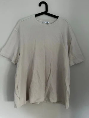 Beige strukturerad t-shirt från Zara - Säljer en beige t-shirt från Zara i storlek M men passar även en L. T-shirten har en ribbad struktur och är tillverkad i mjukt bomullsmaterial. Modellen är kortärmad med rund hals och har en loose passform som ger en chill vibe. Helt ny med prislapp aldrig använd 