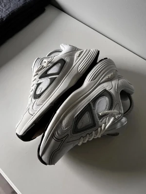 Vita Sneakers - Säljer ett par sneakers i vitt med grå och svarta detaljer. Skorna har en modern chunky sula, meshpaneler och snygga kontrastsömmar. Klassisk snörning och logga på plösen och innersulan. Perfekta för dig som gillar exklusiva och trendiga sneakers. Nästan som nya, bara testade vid ett par tillfällen ✨