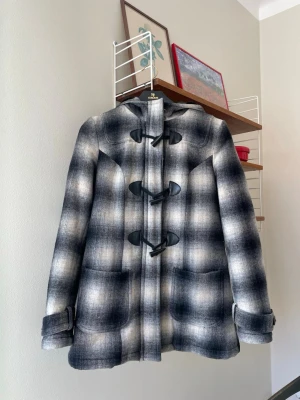 Rutig kappa  - Fodrad jacka med luva. 00-tal. 50 % ull och quiltat foder inuti så den håller värmen väl. Strl 34. Använt men bra skick, se bilder!