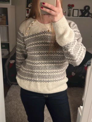 Mönstrad stickad tröja Holly & Whyte - Nypris 399kr. Säljer en mysig stickad tröja från Holly & Whyte med grått och brunt mönster på beige botten. Tröjan har rund hals, lång ärm och fem snygga guldfärgade knappar på axeln. Perfekt för kalla dagar och har en skön loose passform. Väldigt skön!! Använd sparsam. Passar även S💗