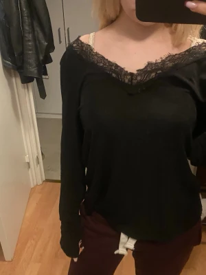 Svart långärmad topp med spets - Säljer en svart långärmad topp med v-ringad hals och snygg spetsdetalj längs urringningen. Toppen har en lite loose passform och är perfekt för dig som gillar en enkel men ändå chic stil. Materialet känns mjukt och bekvämt mot huden.