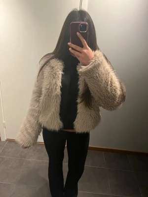 Beige pälsjacka från Gina Tricot XS - Säljer en fluffig och croppad beige pälsjacka från Gina Tricot i storlek XS. Jackan har långärmade ärmar och en riktigt mjuk, lurvig look som ger en cool vibe. Perfekt för dig som vill sticka ut med en trendig jacka i höst och vinter.