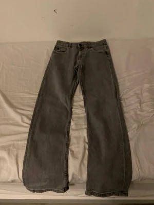 Grå jeans från Kappahl - Säljer ett par gråa jeans från Kappahl i storlek 152. De har en rak och bred passform med klassiska fem fickor och knappgylf. Materialet är slitstarkt jeans och färgen är en snygg mellangrå ton som passar till det mesta.