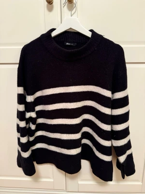 Svartvit randig stickad tröja - Säljer en svart stickad tröja från Gina Tricot i storlek M med breda vita ränder. Tröjan har rund hals och långa ärmar.