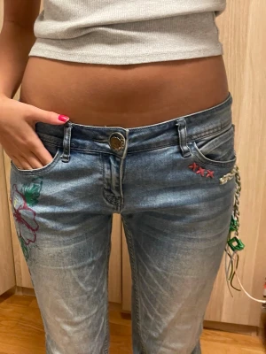 Unika Lågmidjade bootcut jeans  - Unika jeans med blom-detaljer och cool kedja som hänger vid höften! Har sytt ut och upp dem själv men allt annat är orginaldesign! ❤️har oftast 36-38 i byxor och 40 cm ish tvärst över. När jag sydde upp dem gjorde jag det för hand så det går lätt att sprätta upp och göra längre för jag är 165