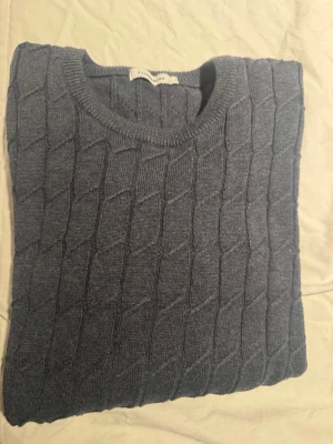 Mörkgrå stickad tröja J.Lindeberg - Säljer en mörkgrå stickad tröja från J.Lindeberg med snyggt kabelstickat mönster. Tröjan har rund halsringning och ribbade muddar vid ärmslut och nederkant. Perfekt för kyliga dagar och enkel att matcha med jeans eller chinos.