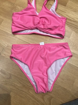 Rosa bikini från SHEIN 11-12 år - Säljer en snygg rosa bikini från SHEIN i storlek 11-12 år. Bikinin har en twistad detalj på toppen och klassiska bikiniunderdelar. Materialet är mjukt och stretchigt syntet, perfekt för strand eller pool. Färgen är starkt rosa och ger en fräsch vibe.