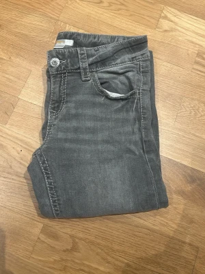 Grå jeans från Gina Tricot, stl 158 - Snygga grå jeans från Gina Tricot i storlek 158. Klassisk femficksmodell med silverfärgade knappar och justerbar midja på insidan. Jeansen har raka ben och tydliga sömmar som ger en cool look. Perfekta för dig som gillar stilrena och enkla jeans.