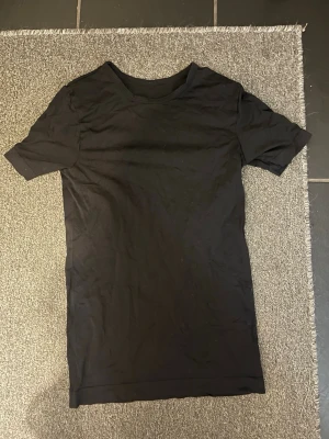 Svart basic t-shirt i bomull - En enkel svart t-shirt med rund hals och korta ärmar. Modellen är rak och har en normal passform, perfekt för en clean och stilren look. Materialet känns mjukt och bekvämt mot huden, troligtvis bomull. Passar dig som gillar minimalistisk stil.