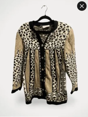 Beige kofta med leopardmönster, strl 38/40 - Unik beige kofta med svart och vitt leopardmönster och grafiska detaljer. Långärmad med svarta kanter och rund halsringning. Perfekt för dig som gillar djurmönstrat och vill sticka ut lite extra.