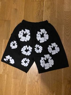 Svart set med vita blommor - Säljer ett svart set med matchande t-shirt och shorts, båda täckta av stora vita blommönster. Setet har en avslappnad passform och elastisk midja på shortsen. Perfekt för dig som gillar statement-plagg och vill sticka ut med en cool och lekfull stil. Passar till dom mesta atorlekarna.kom dm ifall du undrar över något 