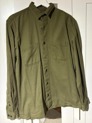 Olivgrön overshirt med fickor - Stilren olivgrön overshirt med två bröstfickor och svarta knappar framtill