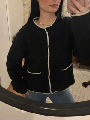 Alpacka/ull stickad kofta❤️ - Mysig svart Alpacka/ull  kofta med vita kontrastkanter och rund hals. Koftan har knappar framtill och två fickor med vit kant. Modellen är loose fit och har långärmade ärmar. Materialet är stickat och känns fluffigt och mjukt. Strl L men passar perfekt på mig som är xs/s❤️