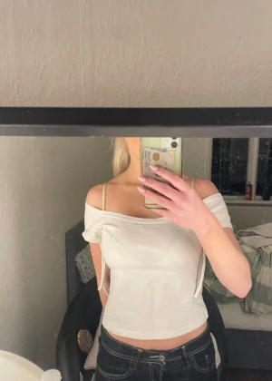 Topp från Brandy Melville - Söt vit offshoulder topp/t shirt från Brandy Melville  Storleken är onesize men skulle säga att den är som en xs/s  Lite småfläckar på ryggen som syns på bilderna men det är absolut inget man lägger märke till (tror banden är till för att knyta runt armarna så den inte åker upp)