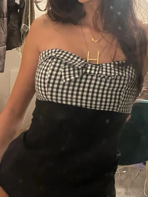 Vintage Rutig bandeau topp med rosett - Säljer en snygg bandeau topp med svartvitt rutigt mönster upptill och en söt rosett framtill. Det är en n klänning egentligen men jag använder den som topp, det går lika bra!🙏🏼🥰 inbyggda ”kupor” så Man kan ha den helt själv. Dragkedja baktill, den är lite trög men den funkar som den ska 🙏🏼