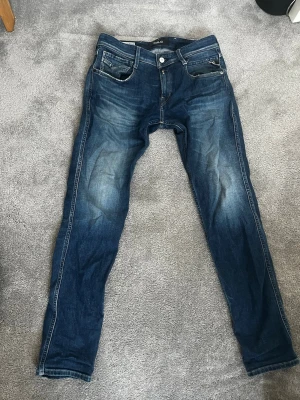 Replay anbass jeans  - Säljer ett par blå Replay jeans med snygg tvätt och klassiska fem fickor. Jeansen har slim passform och raka ben, med Replay-lapp bak i midjan. Perfekta för dig som gillar en modern och stilren look.