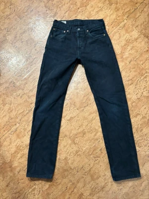 Levi's 501 mörkblå raka jeans - Klassiska Levi's 501 jeans i svart tvätt med raka ben och femficksmodell. Jeansen har knappgylf och den ikoniska läderlappen bak i midjan. Perfekta för dig som gillar tidlös stil och vill ha ett par jeans som funkar till allt.