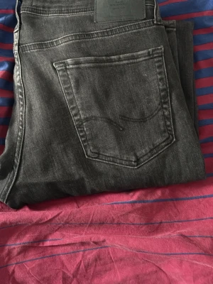 Svarta Jack and Jones jeans - Snygga svarta jeans i klassisk slim modell. Jeansen har fem fickor, normal passform och är tillverkade i mjukt bomullsjeansmaterial. Perfekta för dig som gillar en stilren och enkel look. W32 L34