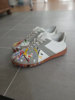 Snygga maison margiela paint splater - Säljer ett par vita och grå sneakers med coola färgstänk. Skorna är dålig kvalitet. Säljer de biligt efteraom de nog inte är äkta. Pris kan diskuteras och hör av er om ni har några frågor😁