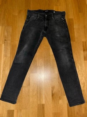 Replay svarta jeans - Strl: 32-30.  Passar även 30-30 Snygga svarta jeans från Replay med smal passform och klassisk femficksdesign. Jeansen har diskreta slitningar och en mörk tvätt som ger en cool look. Perfekta för dig som gillar stilrena och moderna jeans.