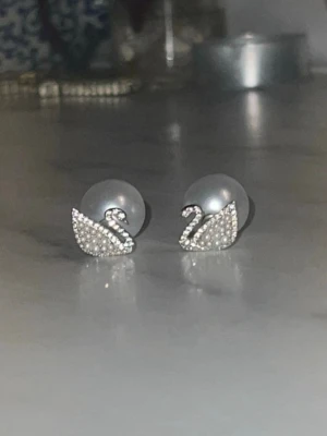 Svanformade pärlörhängen med strass - Supersöta örhängen i form av svanar med gnistrande strass och små vita pärlor. Baksidan pryds av en större rund pärla som ger en lyxig känsla. Perfekta för dig som gillar unika och eleganta accessoarer.