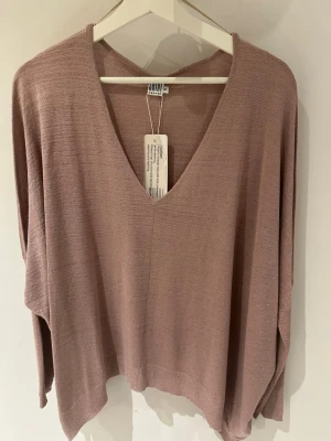 Rosa glittrig stickad tröja Saint Tropez - Trendig rosa glittrig stickad tröja från Saint Tropez med djup V-ringning och avslappnad passform. Tillverkad i ett mjukt, tunt material som ger en snygg siluett. Perfekt att styla med jeans eller kjol för en chill look. Storlek XL men motsvarar M/L. Längd ca 65cm.
