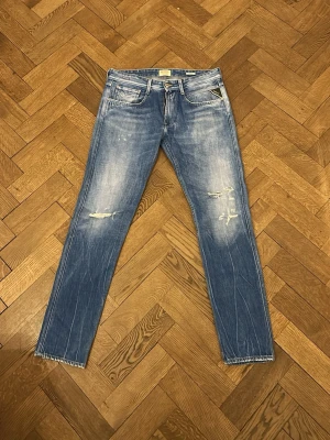 Blå slitna jeans från Nudie Jeans - Snygga blå jeans från replay med slitningar och hål på låren för en cool, avslappnad look. Klassisk femficksmodell med raka ben och ljusa tvättade partier. Perfekta för dig som gillar streetstyle och en trendig vibe. Storlek 32/33.