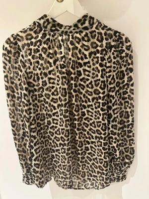 Leopardmönstrad blus med v-ringning storlek S-Ny!! - Snygg och trendig blus med leopardmönster i beige, svart och brunt. Blusen har liten krage och långa ärmar med knappar vid ärmslut. Tillverkad i ett tunt, transparent material som ger en luftig känsla. Knäppning bak (3 knappar). Längd 64cm