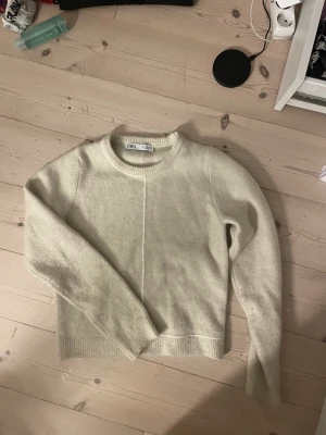 Krämvit stickad tröja från Zara - En stilren krämvit stickad tröja från Zara med rund halsringning och lång ärm. Tröjan har en rak passform och en diskret söm framtill som detalj. Är storlek s men mer som xs 