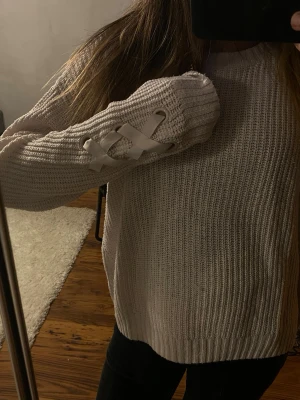 Ljusrosa tröja med snörning - Säljer en ljusrosa tröja med snygg snörningsdetalj i vitt band på ena ärmen. Tröjan har rund halsringning, lång ärm och är gjord i ett mjukt, ribbstickat material. Perfekt för dig som gillar en enkel men trendig look.