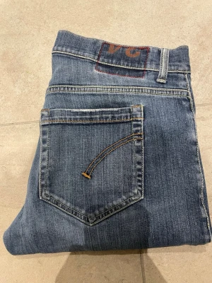 Blå dondup jeans - Snygga blå dondup jeans med klassisk femficksdesign och raka ben. Jeansen har kontrastsömmar och en diskret logga på bakfickan. Perfekta till vardags och passar till det mesta. Tillverkade i slitstarkt denimtyg. Jeans passar någon som bär 34 33 32 i midjan 