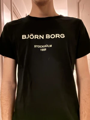 Mörkblå Björn Borg t-shirt - Snygg mörkblå t-shirt från Björn Borg med vit text på bröstet där det står 'BJÖRN BORG STOCKHOLM 1956'. Klassisk passform och rund halsringning. Perfekt till jeans eller shorts för en clean och enkel stil. Hör gärna av dig vid frågor eller liknande🙏