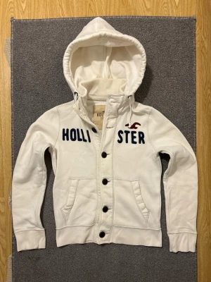 Vintage Hollister Cardigan Med Knappar - Väldigt sällsynt och vintage Hollister hoodie med knappar | Tröjan är i väldigt bra skick utan defekter! | Längd ≈ 63cm, Bredd armhåla-amrhåla ≈ 53cm | Modell 175cm, 68kg | Hör av vid ytterligare frågor och priset kan diskuteras vid snabbt köp! |