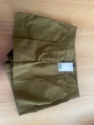 Olivgröna höga skorts i bomull - Snygga olivgröna skorts med hög midja och minimalistisk design. Gjorda i mjuk bomull med en diskret bakficka och rena linjer. Perfekta för varma dagar och enkel att matcha med olika toppar.