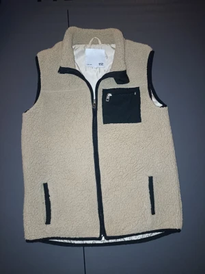 Beige fleeceväst med svarta detaljer - Snygg beige teddyväst med svarta detaljer och dragkedjor. Sitter perfekt. Skulle säga om man är mellan 152 till 155 så sitter den perfekt. Mjuk och varm – perfekt att bära över hoodie eller tröja under höst/vinter eller svala vårdagar. • Bröstficka med dragkedja • Två sidofickor • Dragkedja framtill • Bekväm passform • Fint skick (se bilder) Säljs då den inte kommer till användning. 📦 Kan skickas eller mötas upp. Köparen står för frakt.