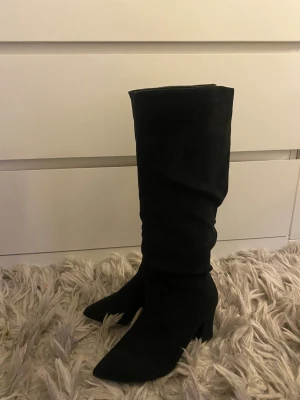 Svarta höga mockastövlar med klack - Snygga svarta stövlar i mocka med klack och spetsig tå. Stövlarna går upp till knäet och har en stilren, enkel design som passar till många outfits. Perfekta för dig som vill ha ett par trendiga boots med lite extra höjd. Priset är alltid förhandlingsbart!!💕