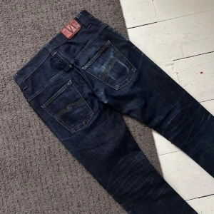 Mörkblåa Nudie Thin Finn Jeans - Riktigt stilrena Nudie Dry Jeans i Thinn Finn modell. | W30 L32 | Riktigt fint skick, liten slitning vid cuffsen som ej syns. Längd: 107cm, Midja: 37-41cm (Stretch). | Väldigt tydliga fades! | Pris ej hugget i sten, skriv vid minsta fundering.