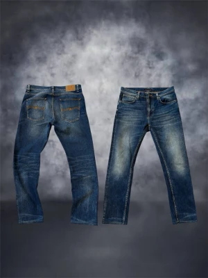 Blå jeans från Nudie Jeans - Säljer ett par klassiska blå jeans från Nudie Jeans med snygg tvätt och raka ben. Jeansen har fem fickor, orangea sömmar och en skinnpatch bak i midjan. Perfekta för dig som gillar en avslappnad men stilren look. Längd är pyttelite kortad