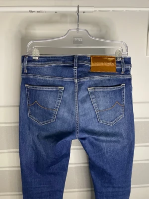 Jacob Cohën jeans - Snygga och exklusiva jeans från Jacob Cohën, modell NICK, i en stilren blå nyans. Kända för sin premiumkvalitet, bekväma passform och lyxiga detaljer. Ett perfekt val för dig som vill kombinera elegans med vardagsstil. 	•	Storlek: W32 	•	Modell: NICK 	•	Färg: Blå 	•	Skick: Mycket bra  Detaljer: ✔️ Tillverkade i högkvalitativ denim ✔️ Bekväma med exklusiv känsla ✔️ Klassisk och tidlös modell som funkar både upp- och nedklätt  Mått (se bild): A: 41.5cm B: 24cm C: 34cm D: 23cm E: 19cm F: 17cm G: 70cm 