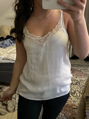 Vit linnetopp med spetsdetalj - Vitt linne med spets detaljer vid toppen. Märket är ”Jaqoueline de yong” men den köpets secondhand. Är i storlek M och är väldigt luftig och sitter inte åt kroppen. Finns inga fläckar eller märken på linnet.