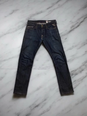 Replay Waitom mörkblå jeans - Säljer ett par klassiska Replay Waitom jeans i mörkblå tvätt. Modellen har en slim/straight, fem fickor och snygga kontrastsömmar. Tillverkade i slitstarkt bomullsjeansmaterial. Perfekta för dig som gillar en clean och tidlös look.
